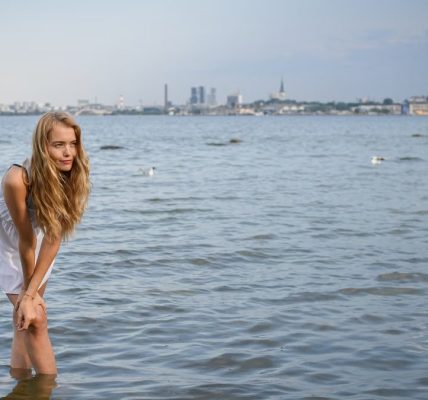 Young woman standing in water with Tallinn skyline in the background on a sunny day.