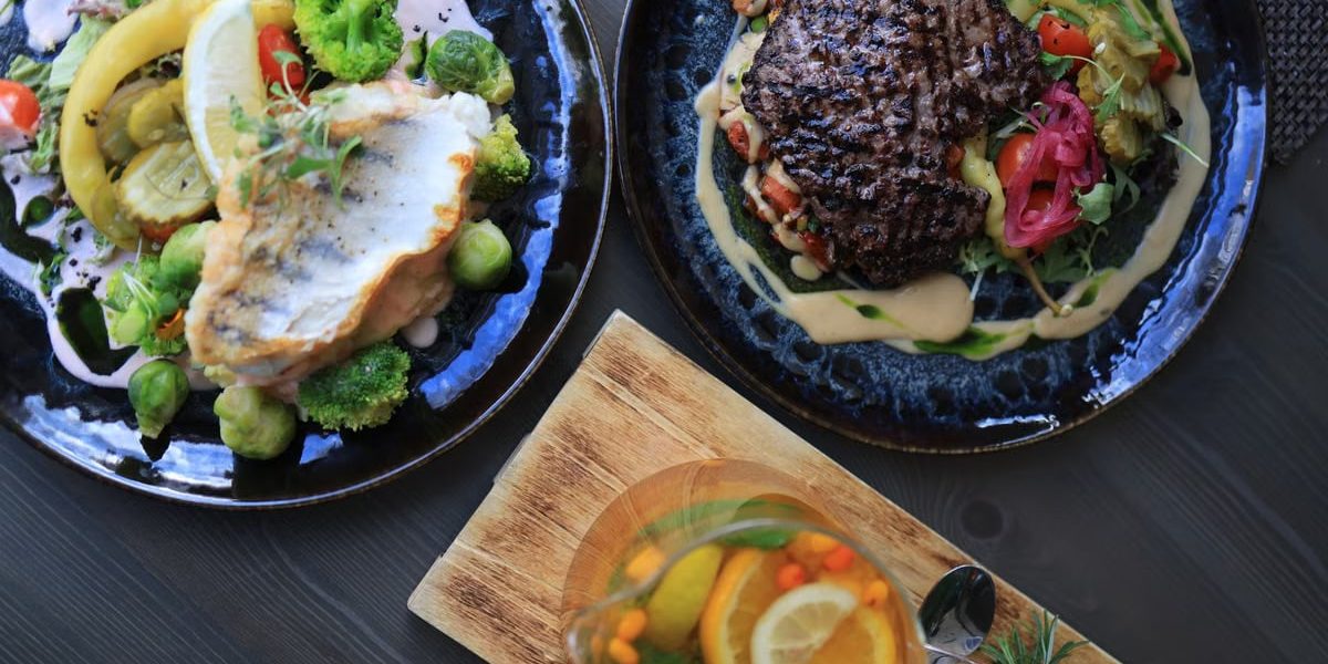 Top view of gourmet fish and steak dishes with fresh citrus and herbs on a stylish table setting.
