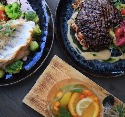 Top view of gourmet fish and steak dishes with fresh citrus and herbs on a stylish table setting.